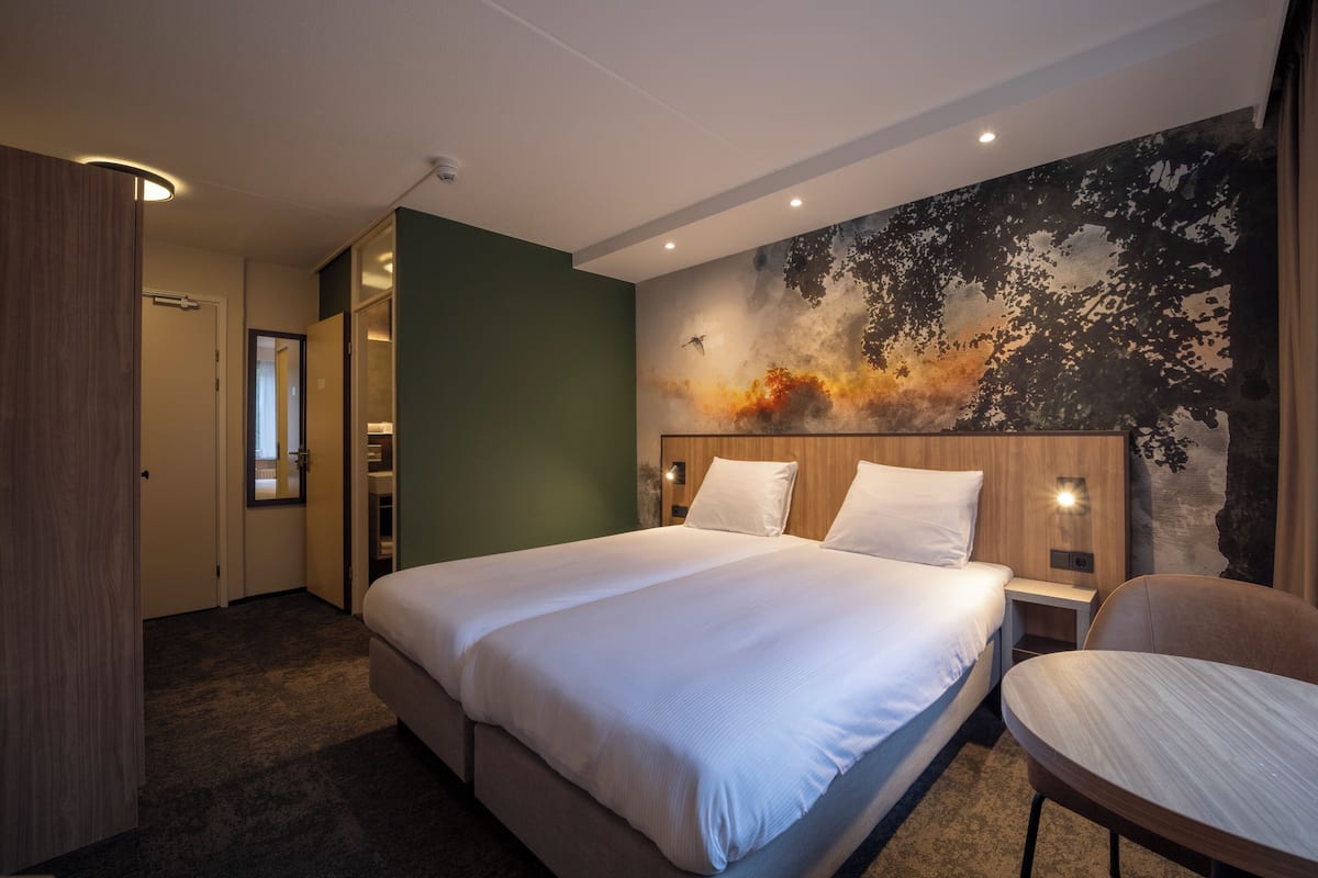 A hotel room with a large bed, a chair, a nightstand, and a wall mural.