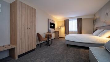Habitación de hotel con cama, escritorio, silla, armario y un amplio ventanal con cortinas.