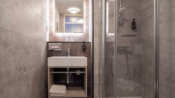 Un baño moderno con cabina de ducha de vidrio, lavamanos con espejo y toallero.