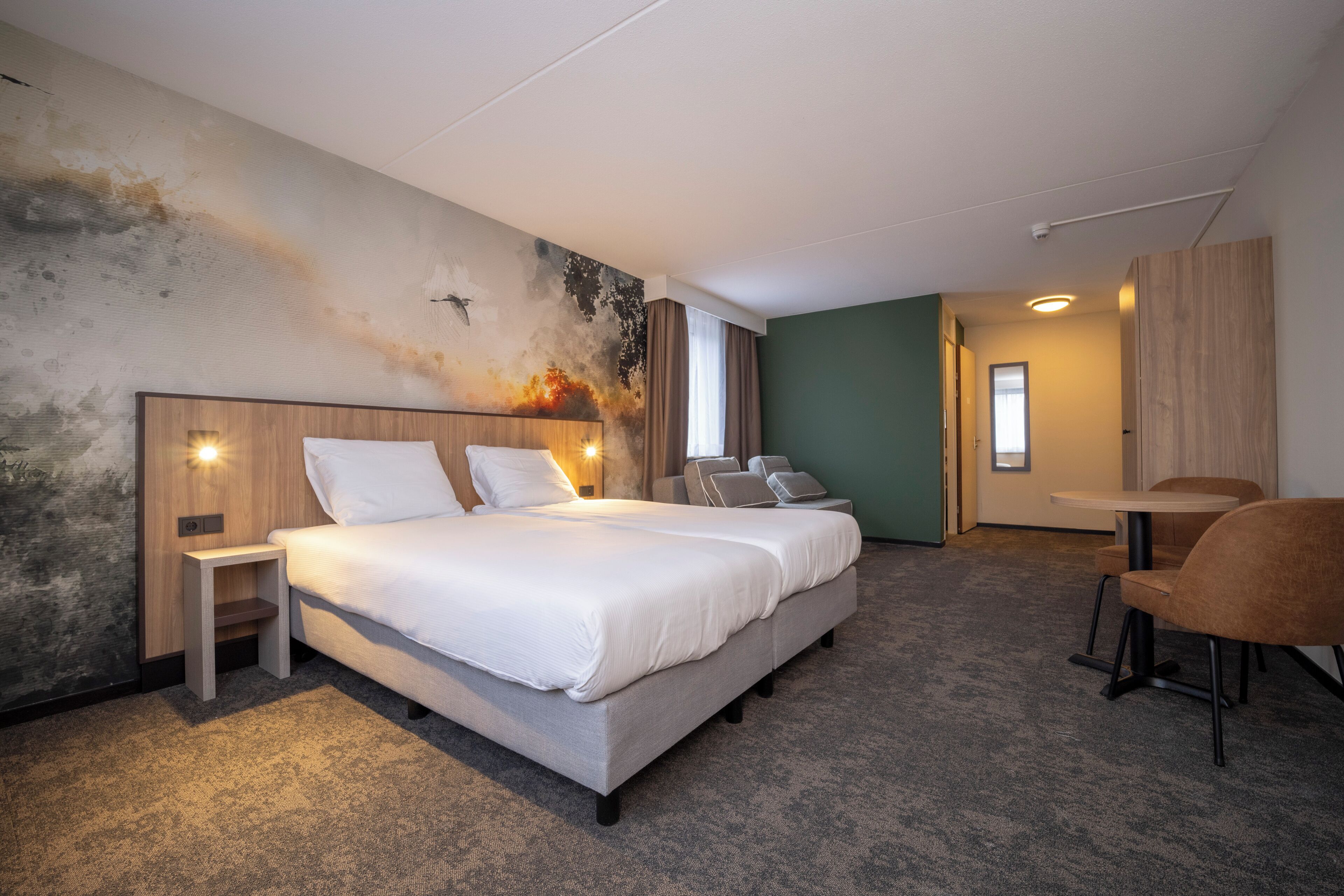 Quarto de hotel moderno com uma cama grande, mesas de cabeceira, uma escrivaninha e uma cadeira.
