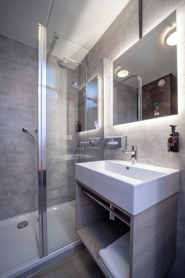 Un baño moderno con ducha de vidrio, un lavamanos blanco y un espejo grande.