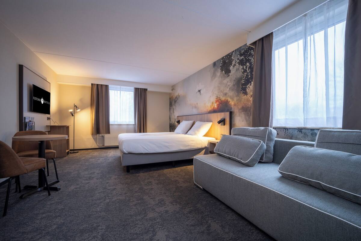 A hotel room with a bed, a sofa, a desk, and a TV.