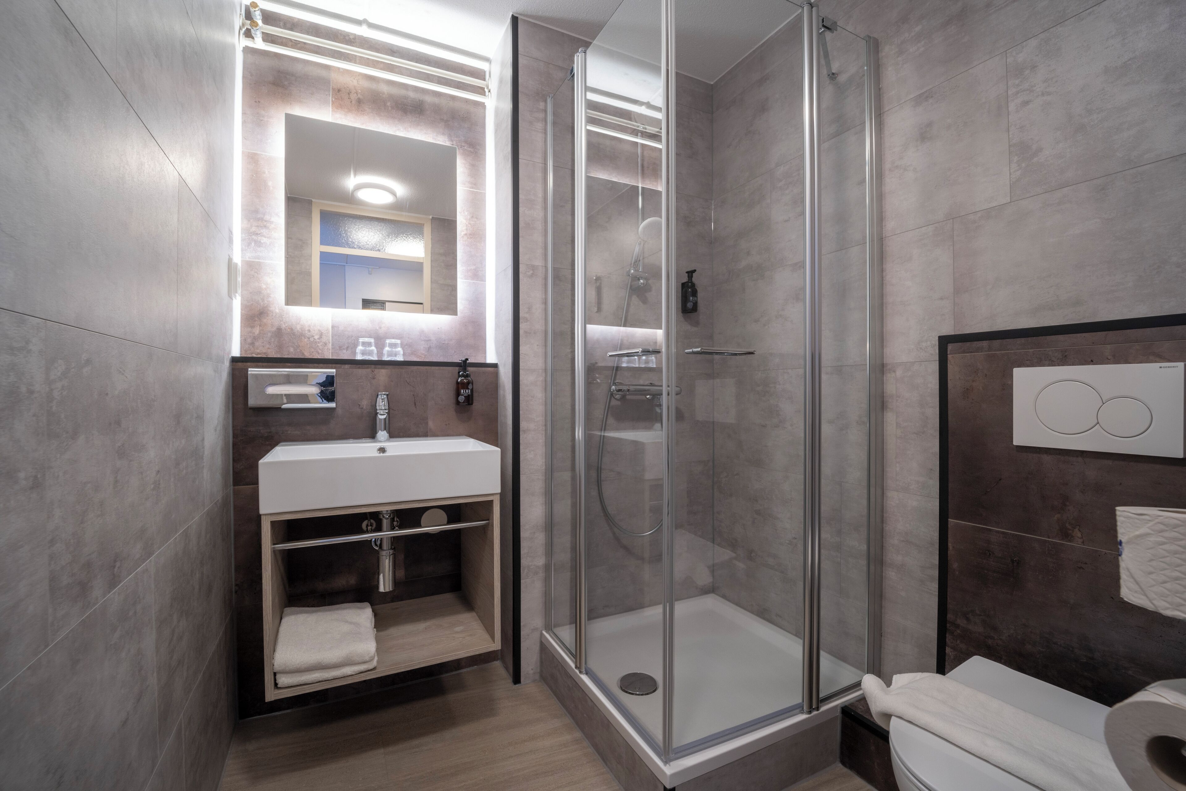 Un baño moderno con cabina de ducha de vidrio, un lavabo con espejo y un inodoro.