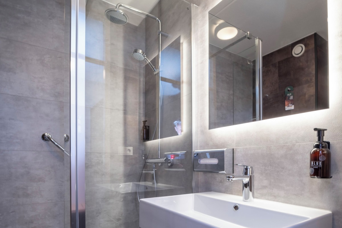 A modern bathroom with a glass-enclosed shower, a white sink, and a large mirror.