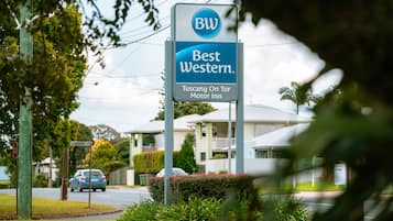 A Best Western sign with a motor inn logo, surrounded by greenery and residential buildings.
