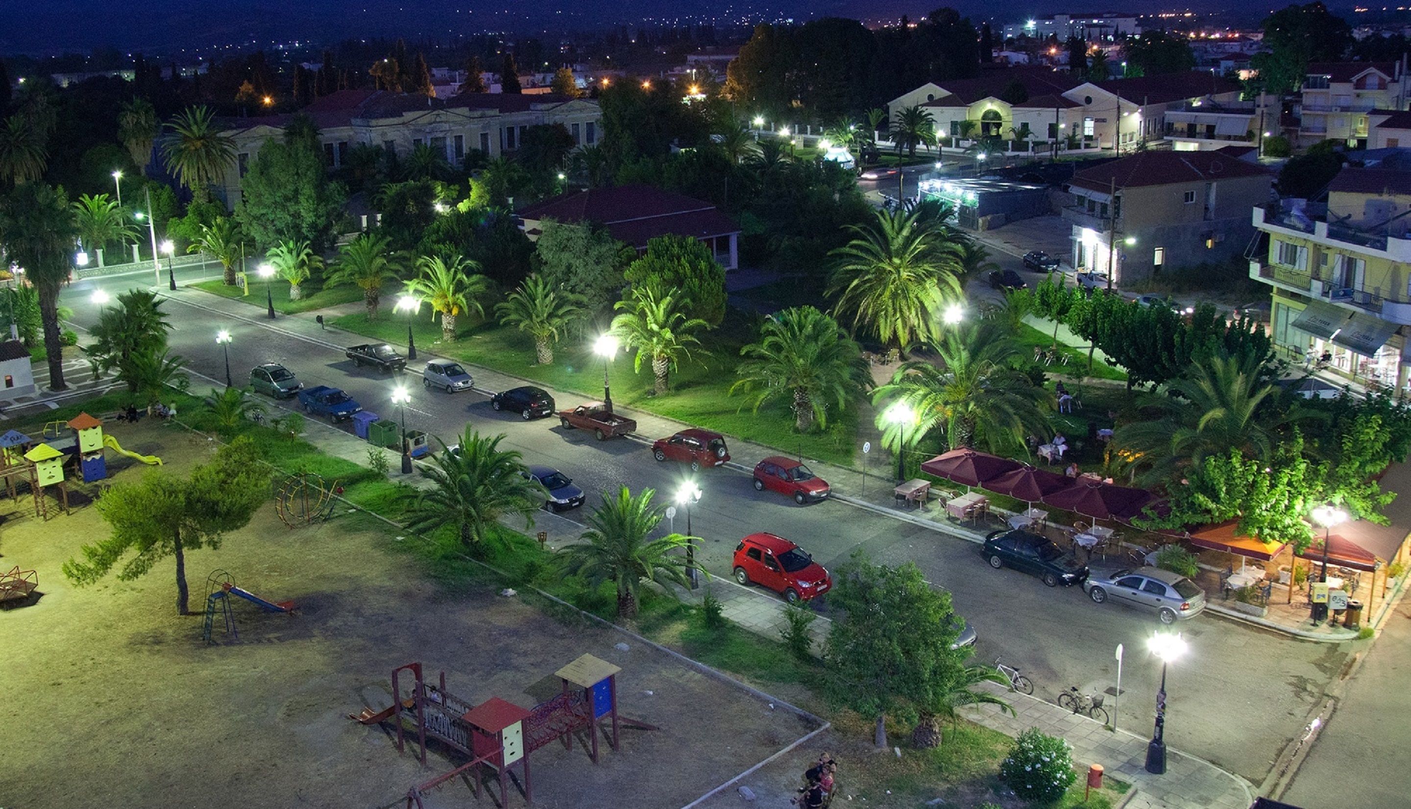 A residential street at night with houses, parked cars, and streetlights.