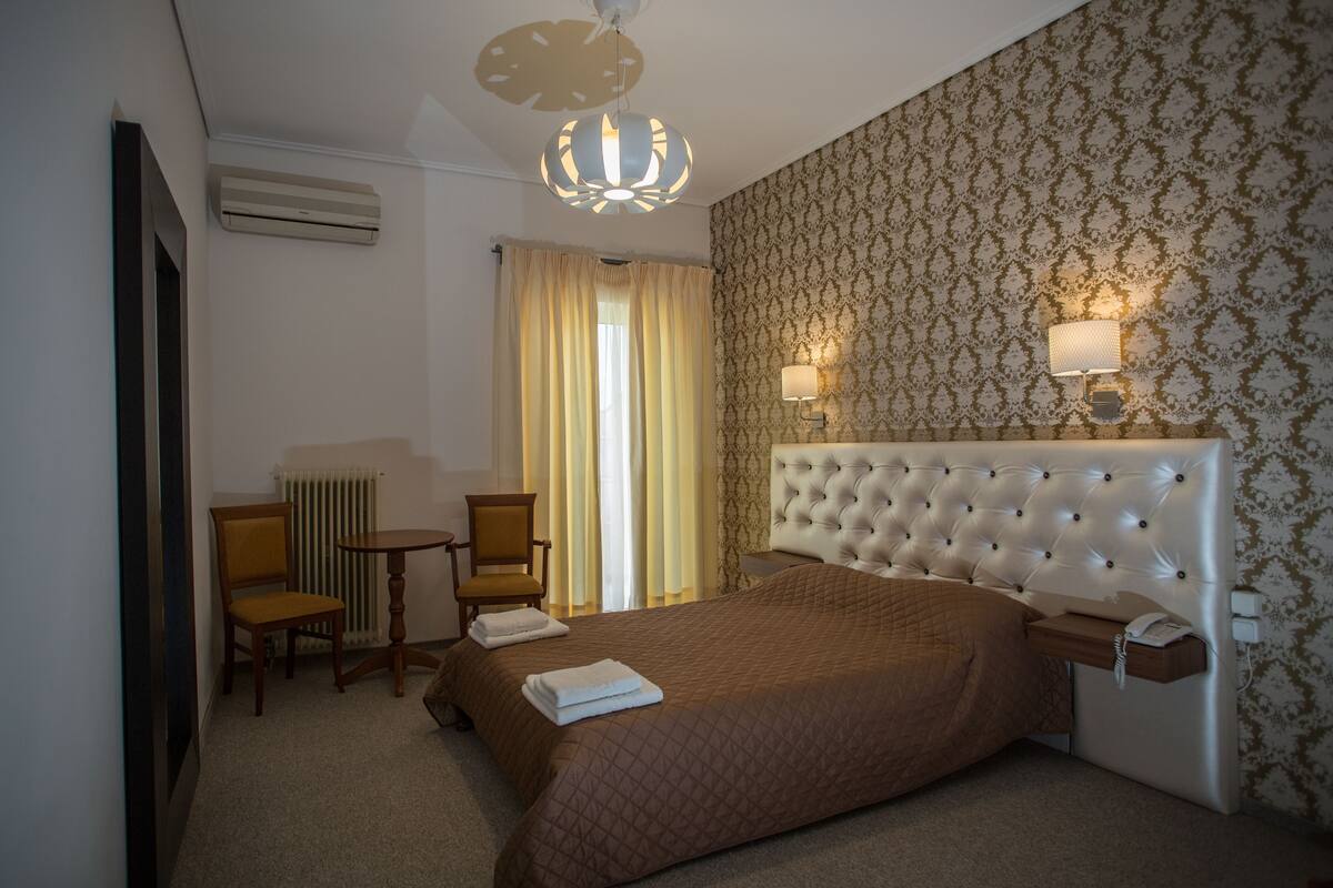 A hotel room with a large bed, a chair, a small table, and a lamp.