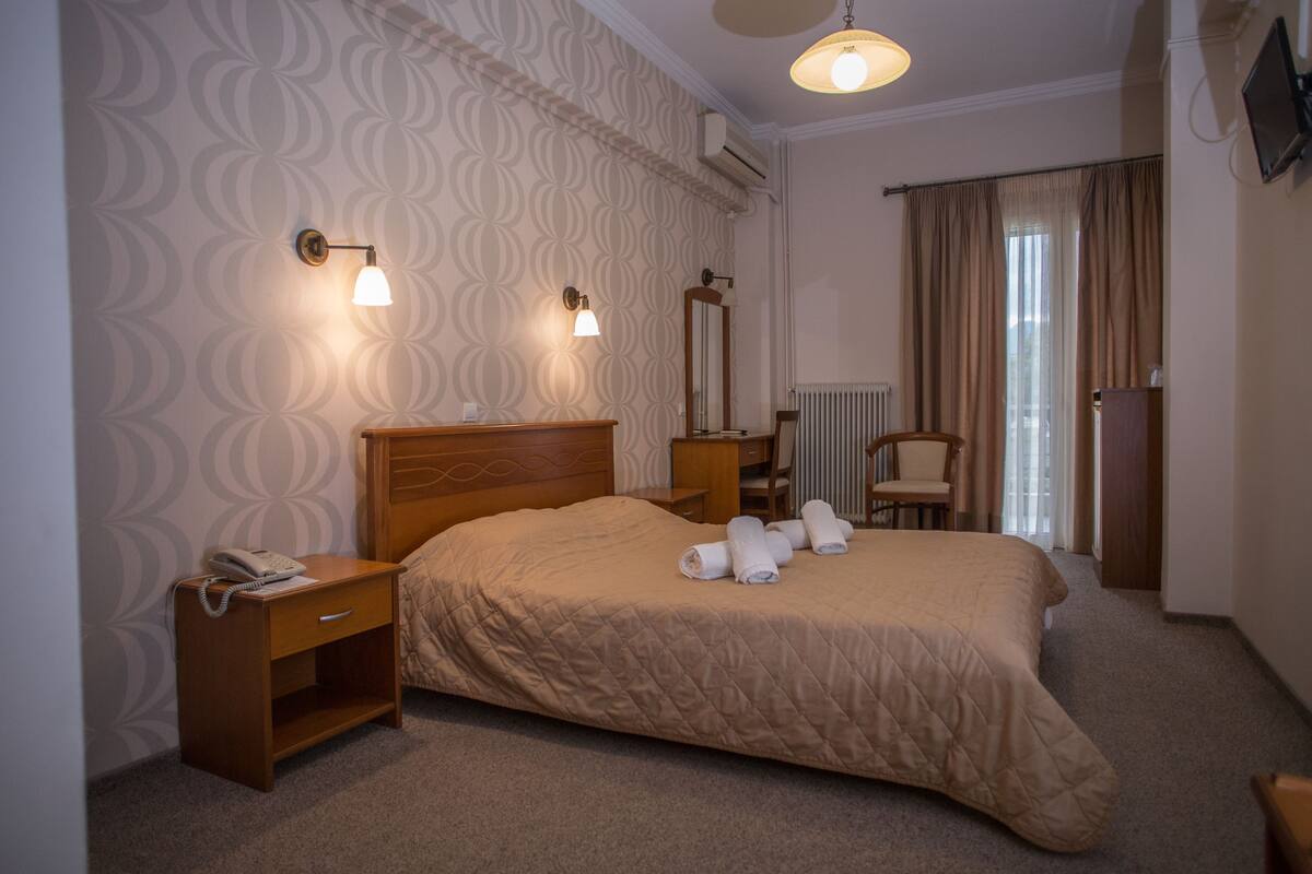 A hotel room with a bed, bedside table with a phone, a chair, a desk, and a mirror.