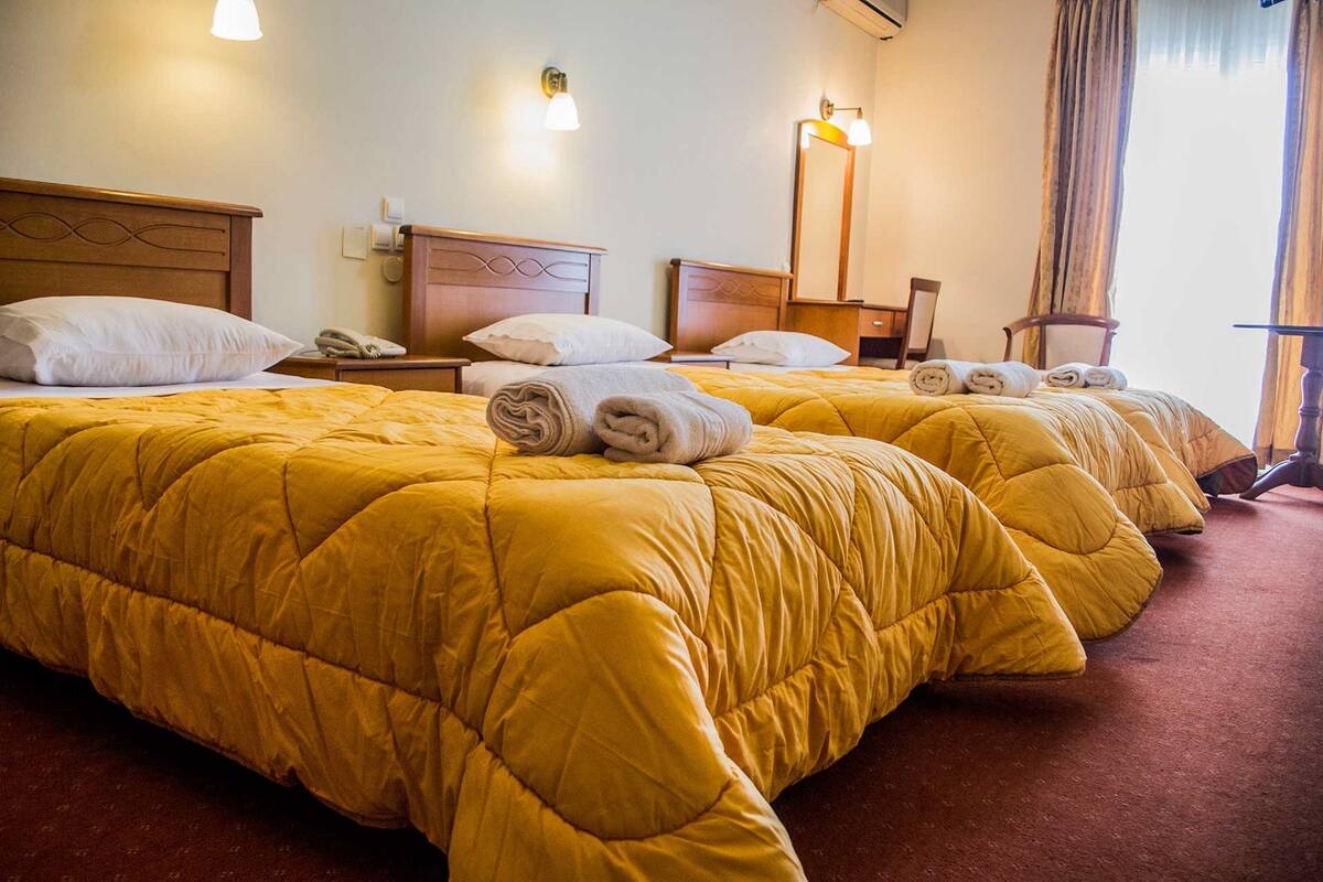 A hotel room with two beds, each with a yellow quilted bedspread and rolled towels.