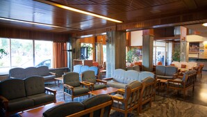 Un vestíbulo espacioso con varias zonas de estar, incluyendo sofás y sillones, dispuestas alrededor de una mesa de centro. Amplias ventanas ofrecen luz natural y vistas al exterior.