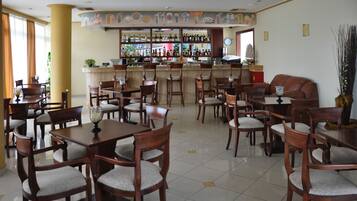 A restaurant with wooden tables and chairs, a bar area with bottles, and a ship model on the wall.