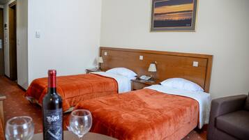 A hotel room with two beds, a wooden headboard, a painting on the wall, and a bottle of wine on a table.