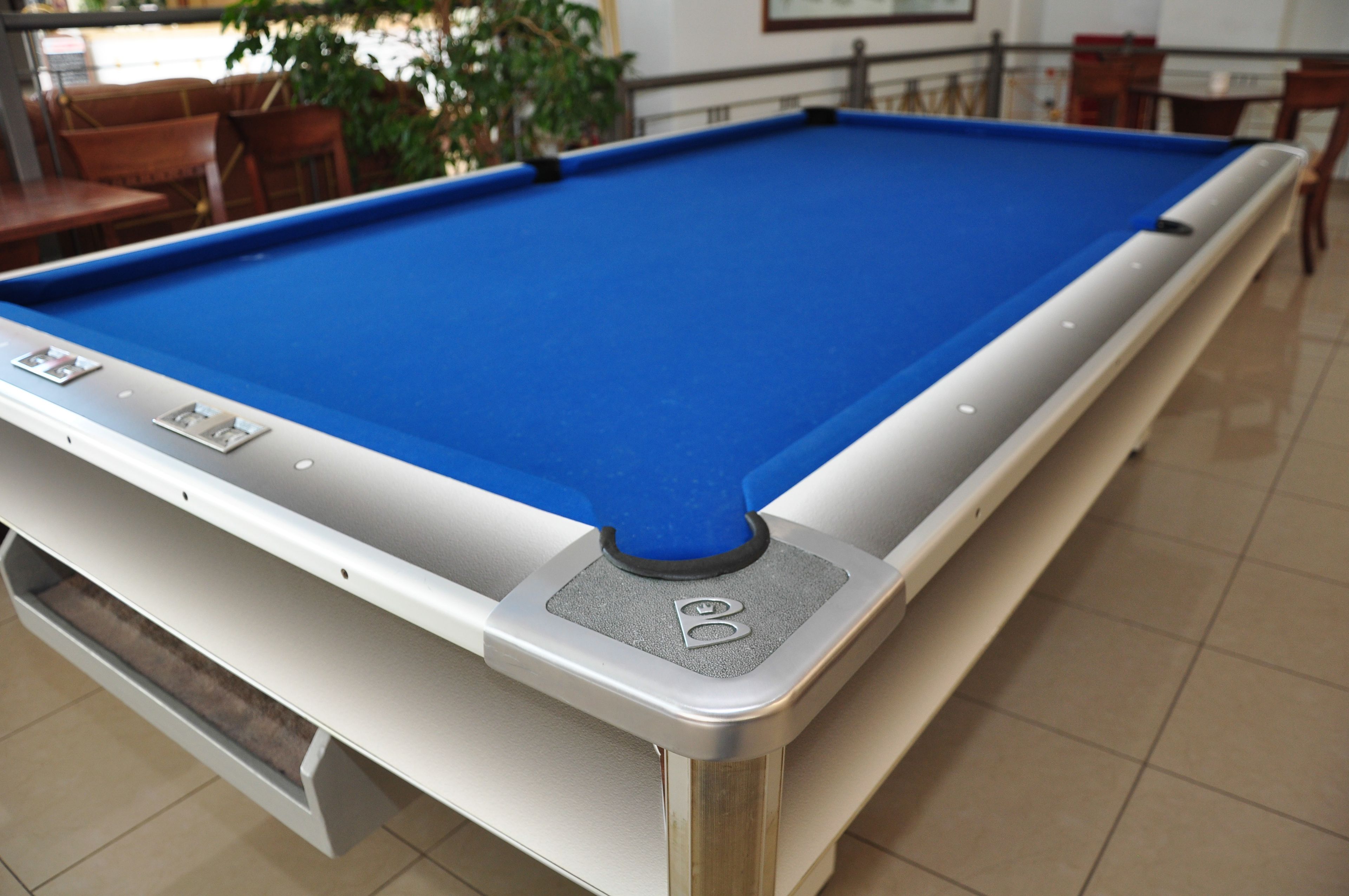Una mesa de billar con superficie de fieltro azul y borde blanco.