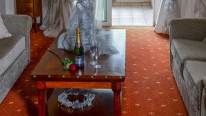 Una habitación con una mesa de madera, un jarrón con flores, una botella de champán y vistas a un balcón con una montaña al fondo.