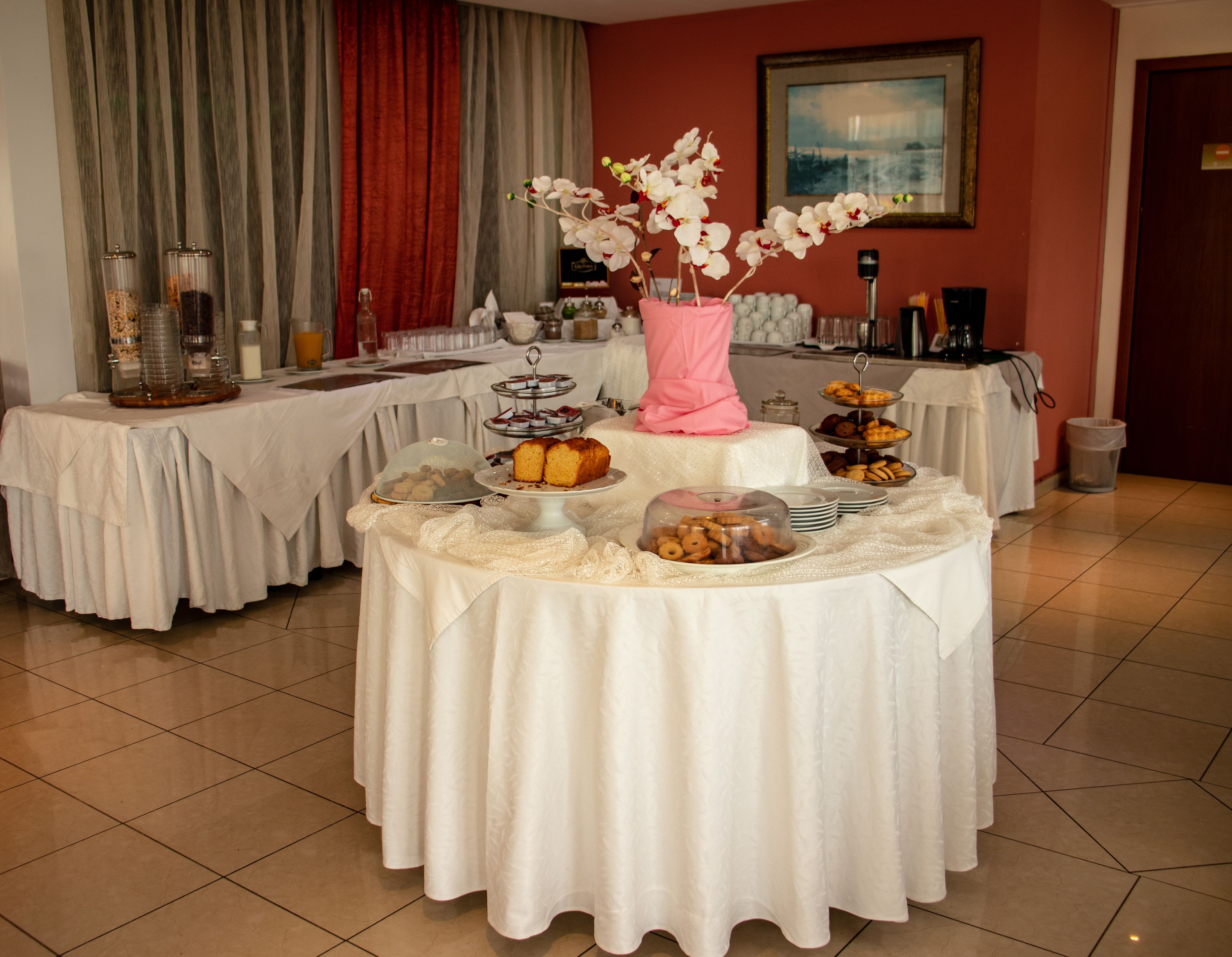 A buffet setup with various food items and a pink vase with white flowers.