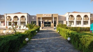 Entrada de un hotel con un camino de piedra que lleva a la puerta, rodeada de vegetación y sillones de descanso.