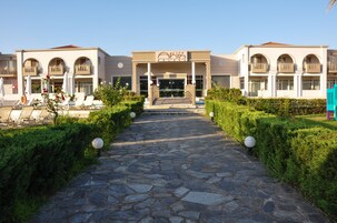 Entrada de un hotel con un camino de piedra que lleva a la puerta, rodeada de vegetación y sillones de descanso.
