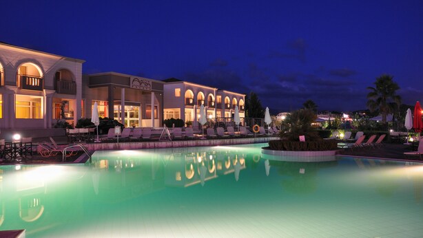 Un hotel con piscina, mobiliario exterior y fachada bien iluminada.