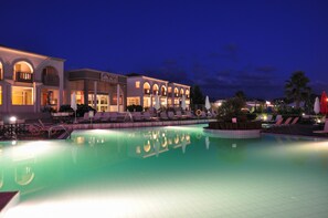 Un hotel con piscina, mobiliario exterior y fachada bien iluminada.