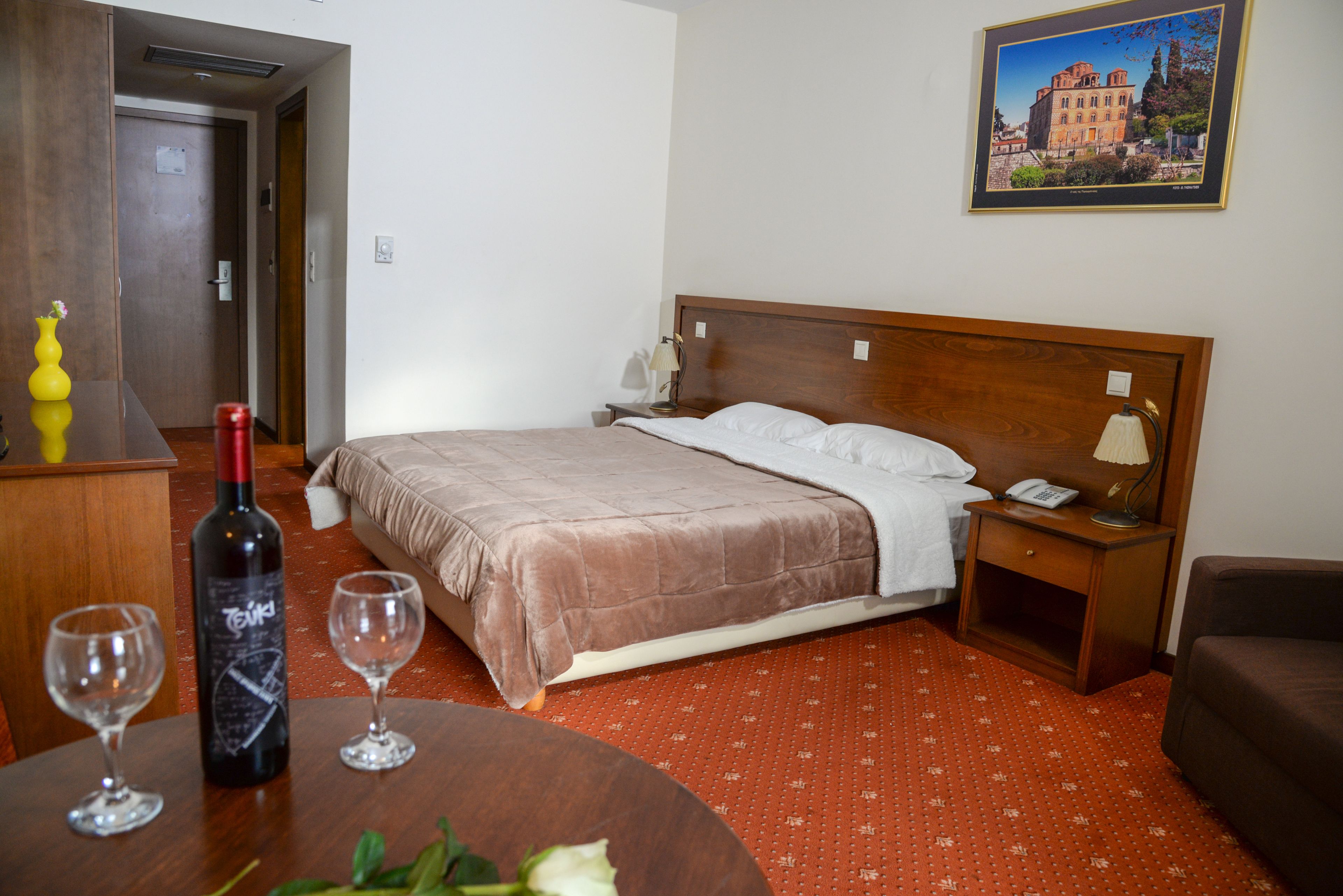 Quarto de hotel com cama, mesa de cabeceira, abajur e uma garrafa de vinho.