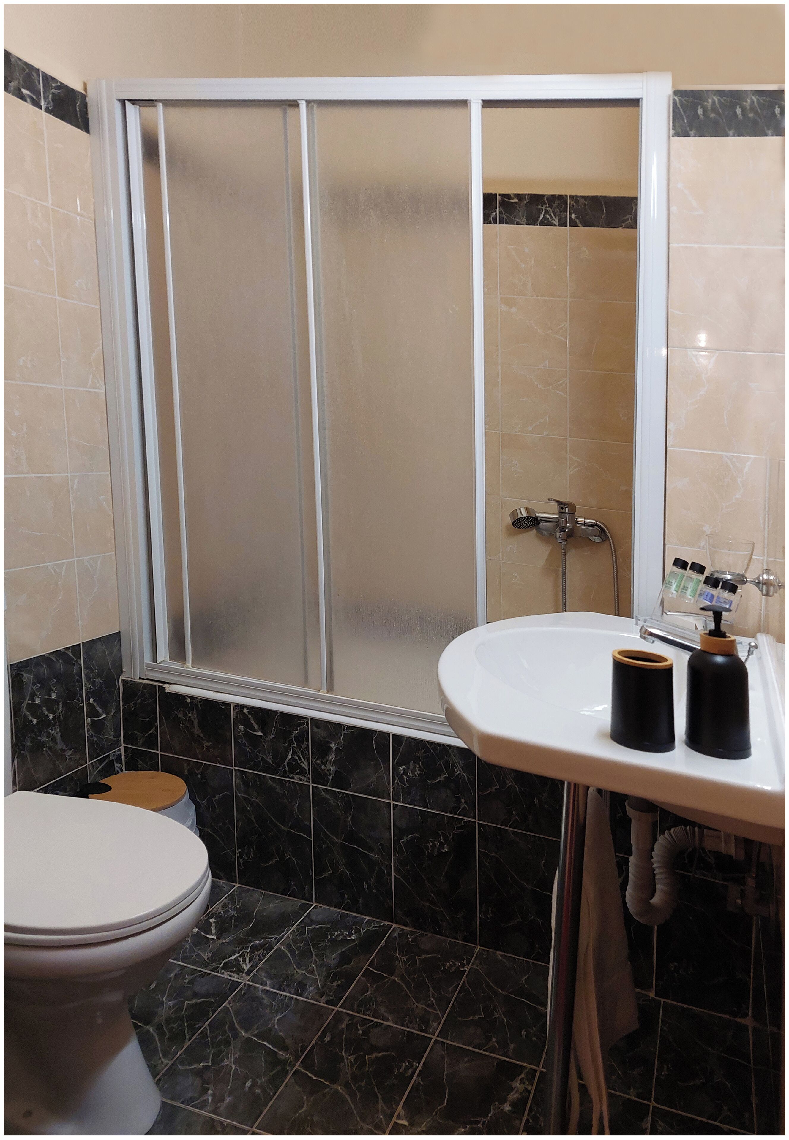 A bathroom with a shower enclosure, toilet, sink, and marble tiles.