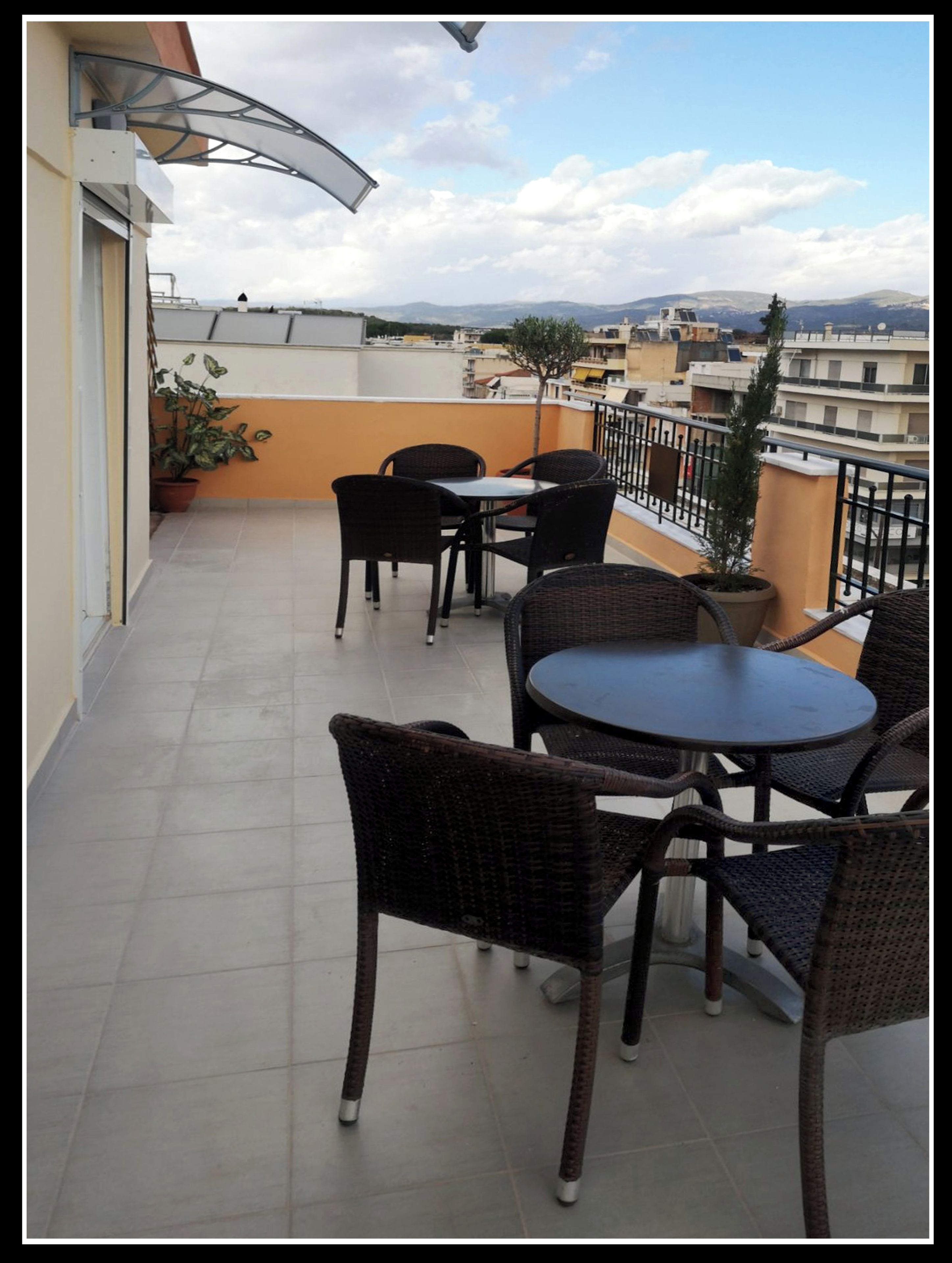 A rooftop terrace with wicker furniture, potted plants, and a view of the cityscape.
