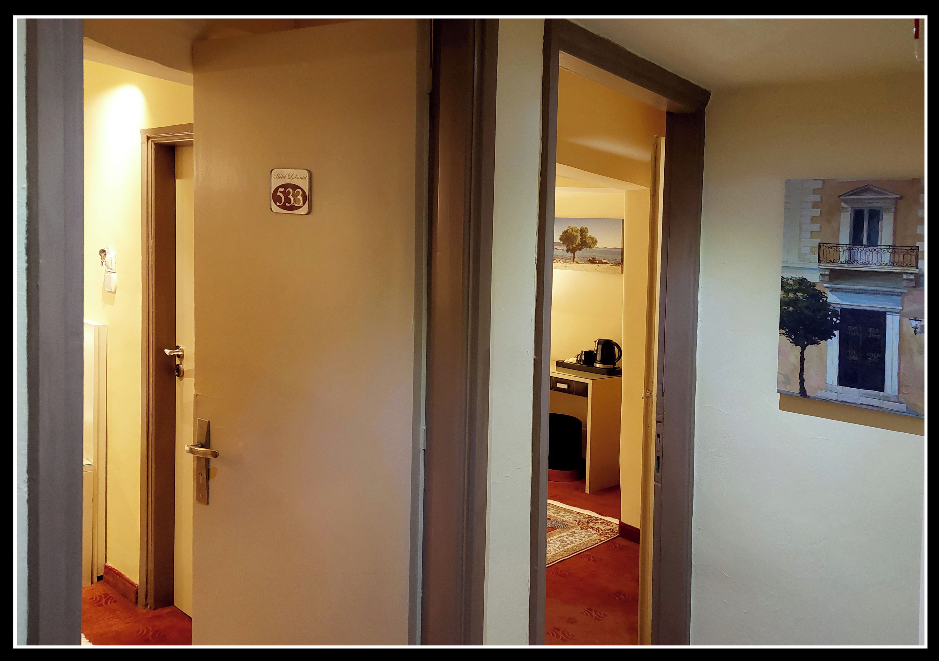 A hallway with a door labeled "533" leading to a room with a window and a painting of a building.
