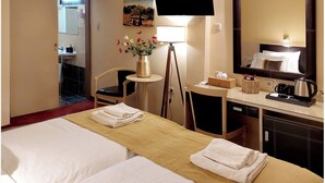 Una habitación de hotel con cama, escritorio, silla, televisión, espejo y un jarrón con flores.