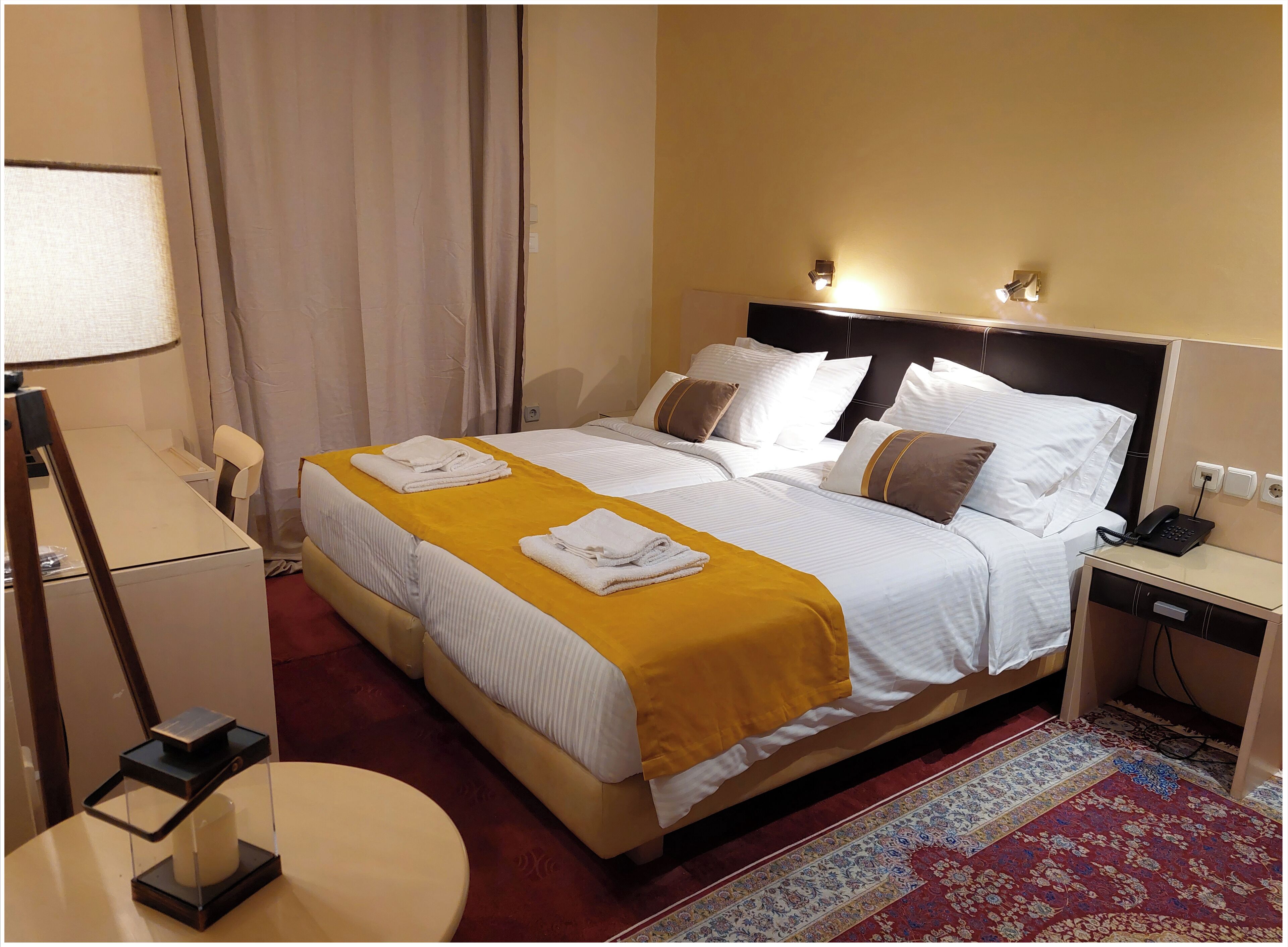 A hotel room with two beds, a desk, a chair, a lamp, a phone, and a decorative rug.