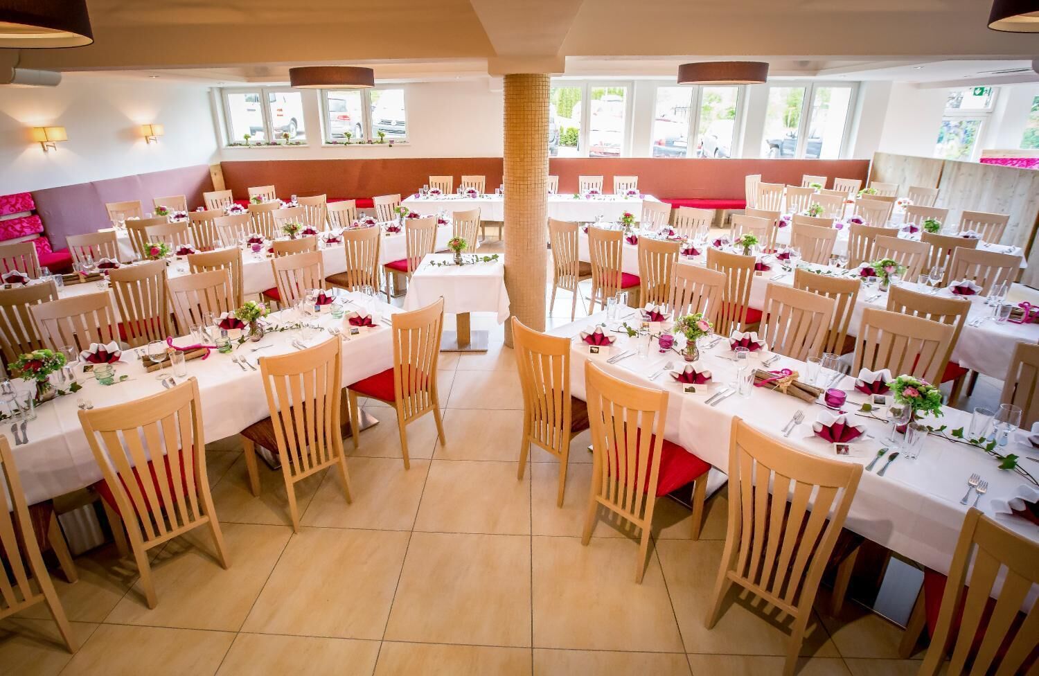 Un amplio comedor con varias mesas redondas, cada una con mantel blanco, cojines rojos y centros de mesa florales.