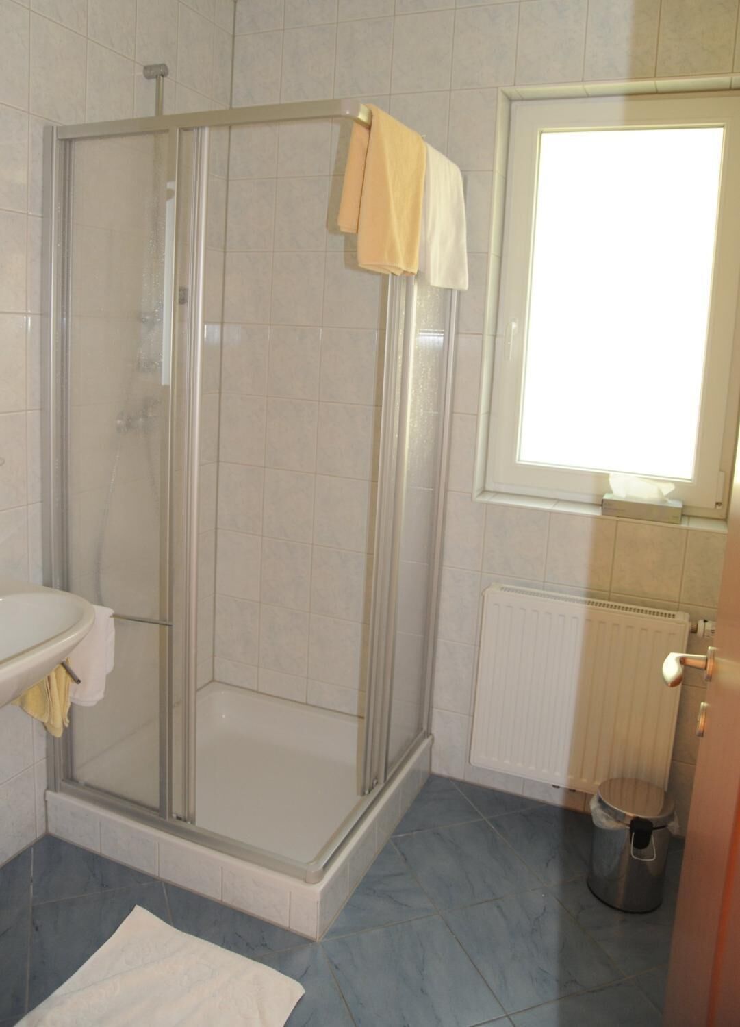 A bathroom with a glass shower enclosure, a white sink, a window, and a radiator.