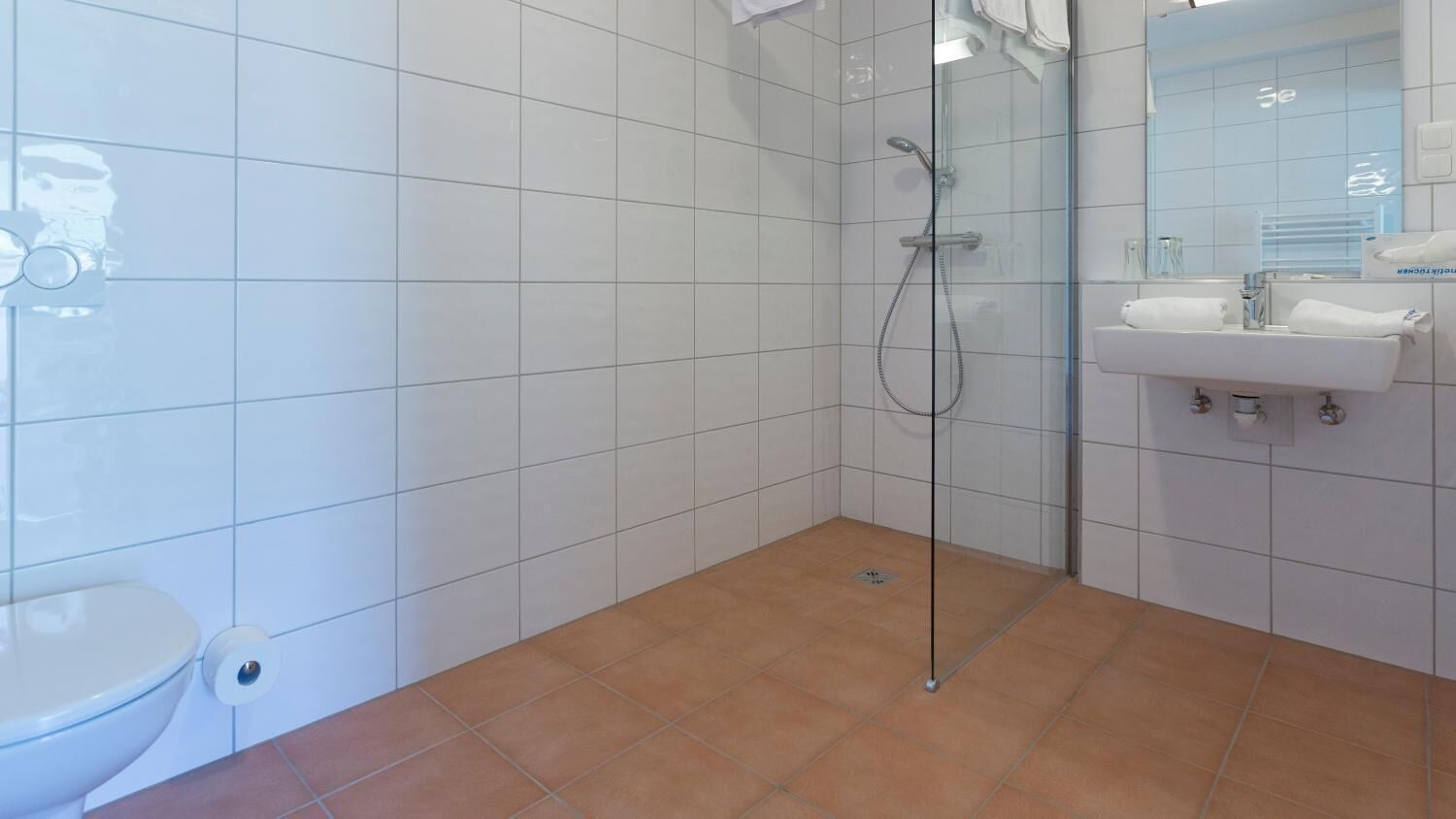 A bathroom with white tiled walls, a glass shower enclosure, a white sink, and a toilet.