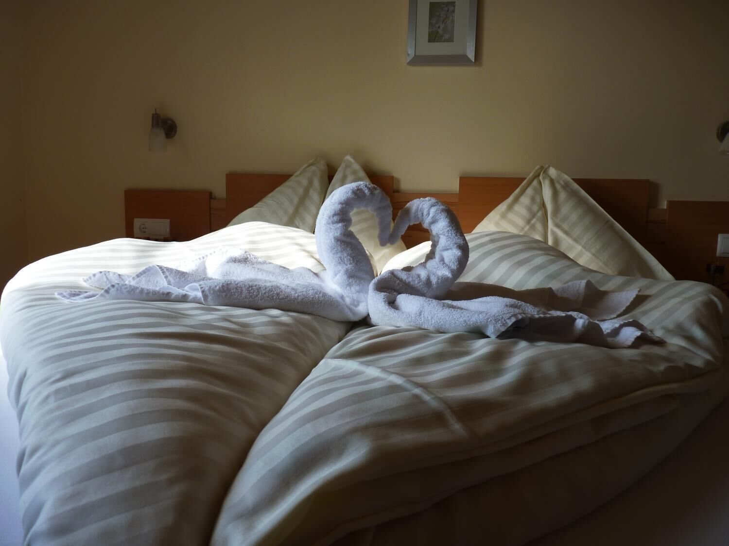 A hotel room with a bed featuring a heart-shaped towel arrangement.