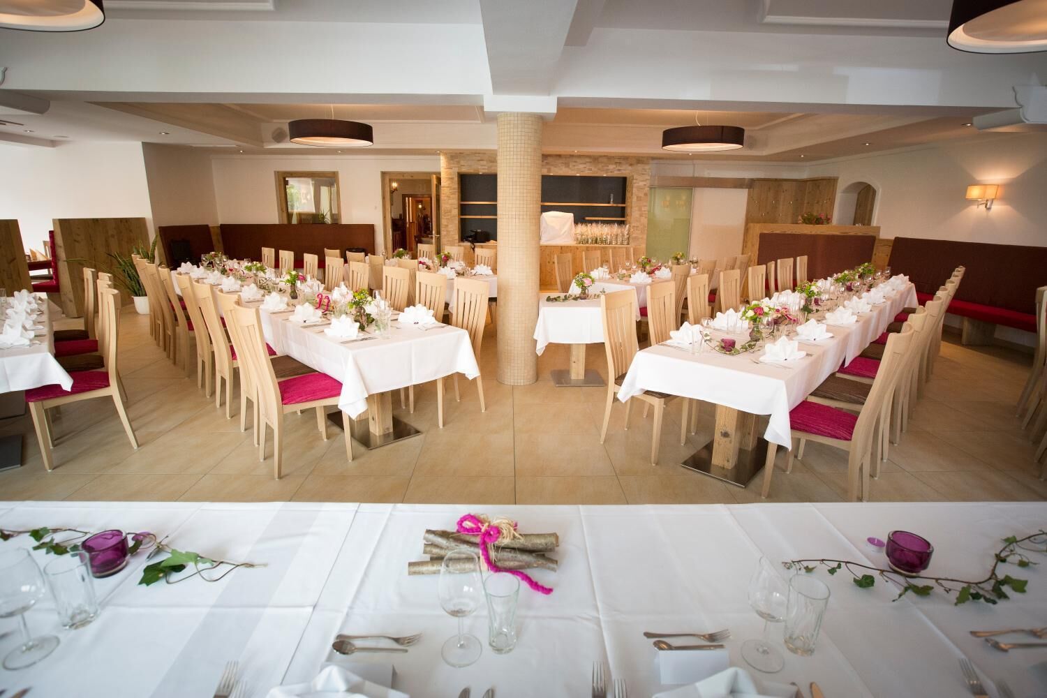 A banquet hall with multiple round tables set for dining, featuring white tablecloths and wooden chairs.