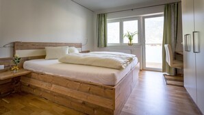A modern bedroom with a wooden bed, a nightstand, a window with curtains, and a view of the outdoors. - Gasthof zur Post (Ossiach)