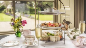 A three-tiered tea service set on a table with floral-patterned cups and saucers, a vase with flowers, and a teapot. - Washingborough Hall Hotel (Lincoln)