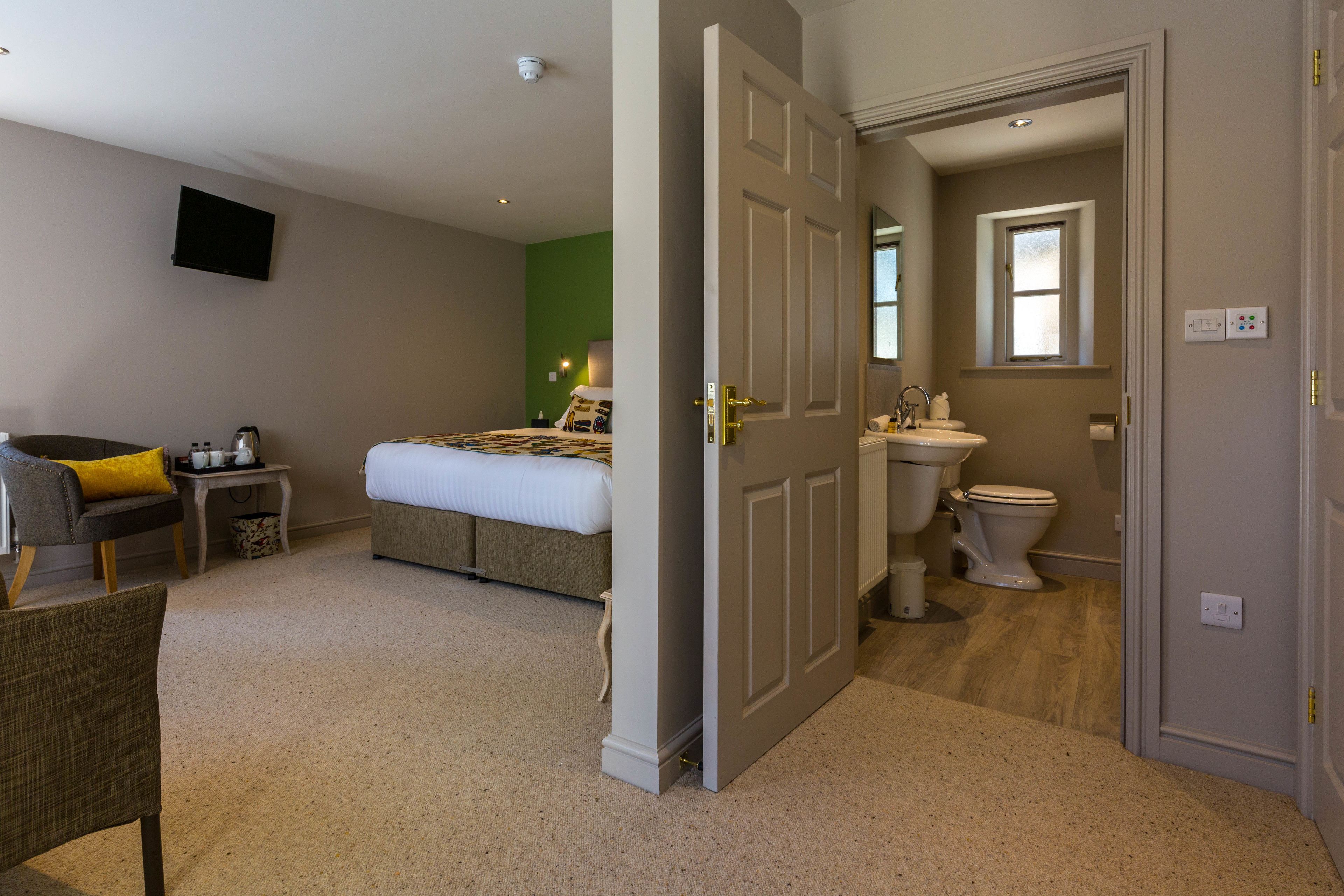 Une chambre à coucher comprenant un lit, une chaise, une petite table avec une lampe et un téléviseur fixé au mur.