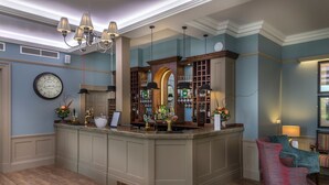 A bar area with a wooden counter, a clock, and a seating area with a chair. - Washingborough Hall Hotel (Lincoln)