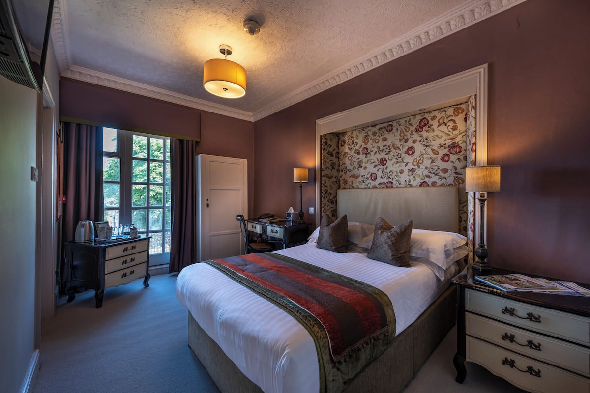 A bedroom with a large bed, a desk with a chair, a lamp, and a window with curtains.