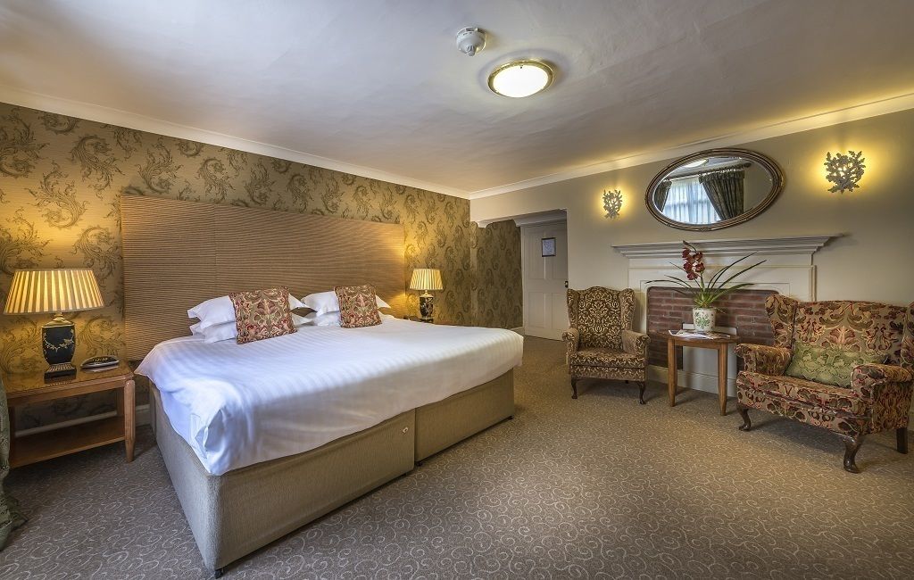 A spacious bedroom with a large bed, two bedside tables, a chair, a sofa, and a fireplace.