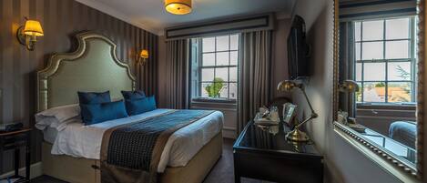 Une chambre d’hôtel avec un grand lit, des lampes de chevet, un bureau avec un miroir et une fenêtre avec des rideaux.