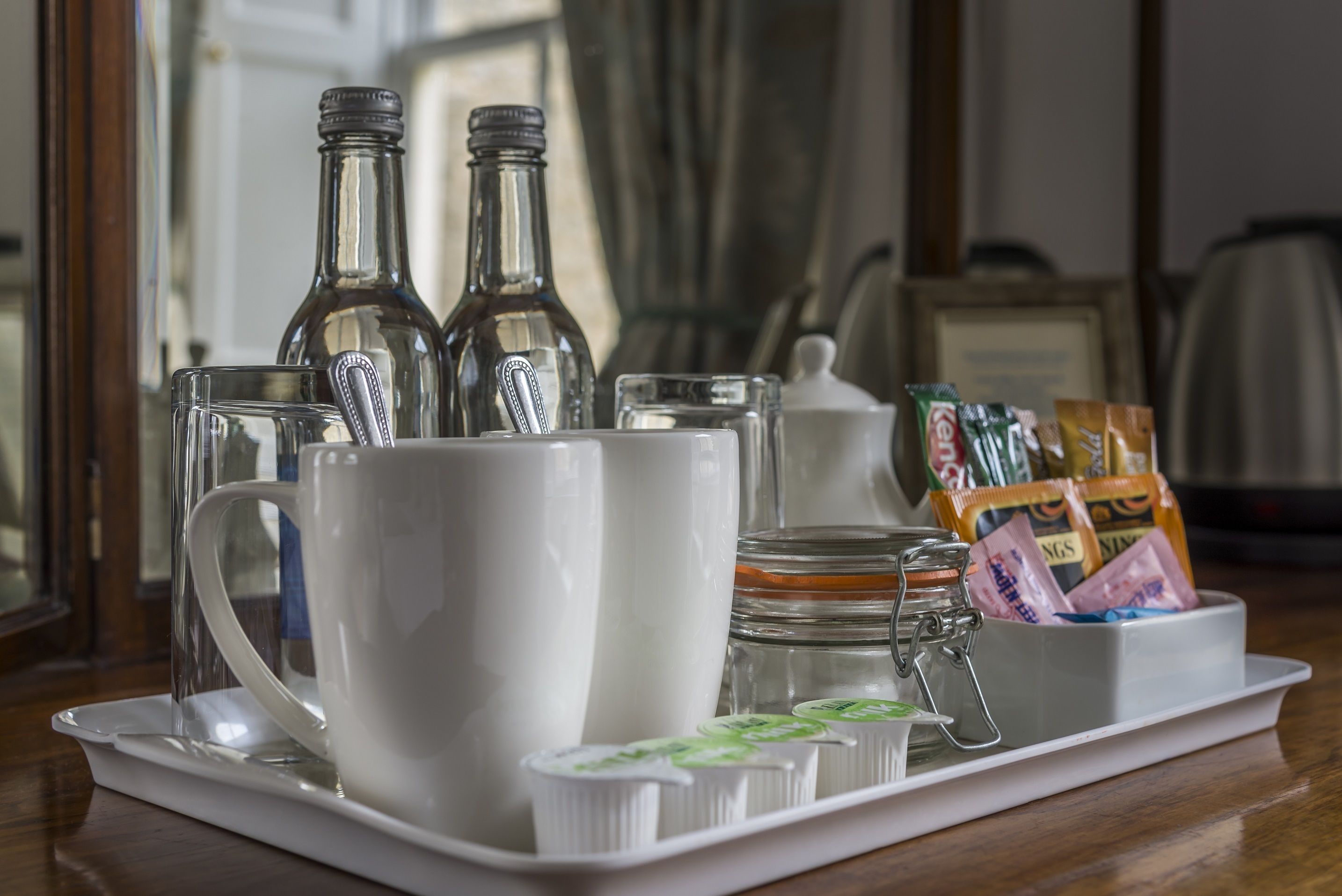 Un plateau sur lequel se trouvent une tasse blanche, deux bouteilles en verre, un bocal en verre et un récipient contenant des sachets, le tout posé sur une table en bois.