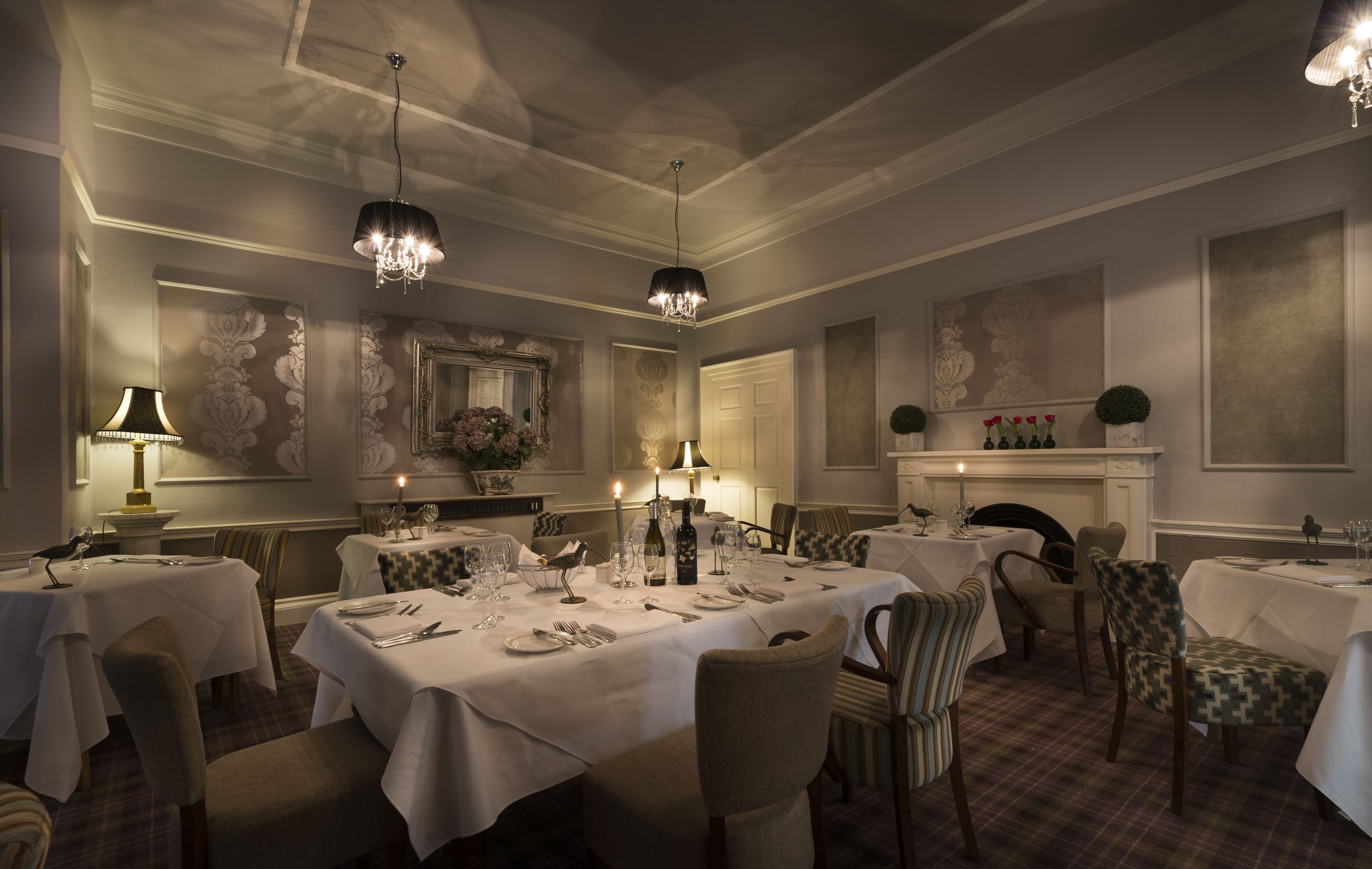 A formal dining room with multiple tables set for service, elegant chandeliers, and classic wall decor.