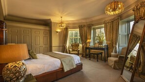 A spacious bedroom with a large bed, a sitting area with a table and chairs, a mirror, and a window with curtains. - Washingborough Hall Hotel (Lincoln)