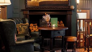 A cozy room with a fireplace, a leather armchair, a small table with a vase, and a painting above the mantel. - Westgate Winchester (Winchester)