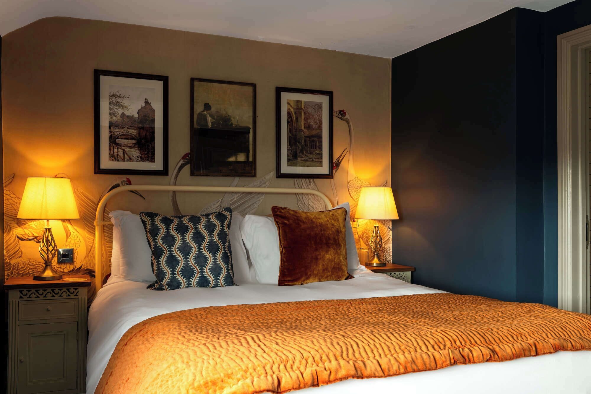 Una habitación de hotel con una cama grande, dos lámparas de noche, un cabecero con tres cuadros enmarcados y una mesita de noche con lámpara.