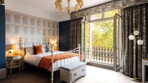 A bedroom with a bed, bedside tables, a bench, a chandelier, and a window with a view. - Westgate Winchester (Winchester)