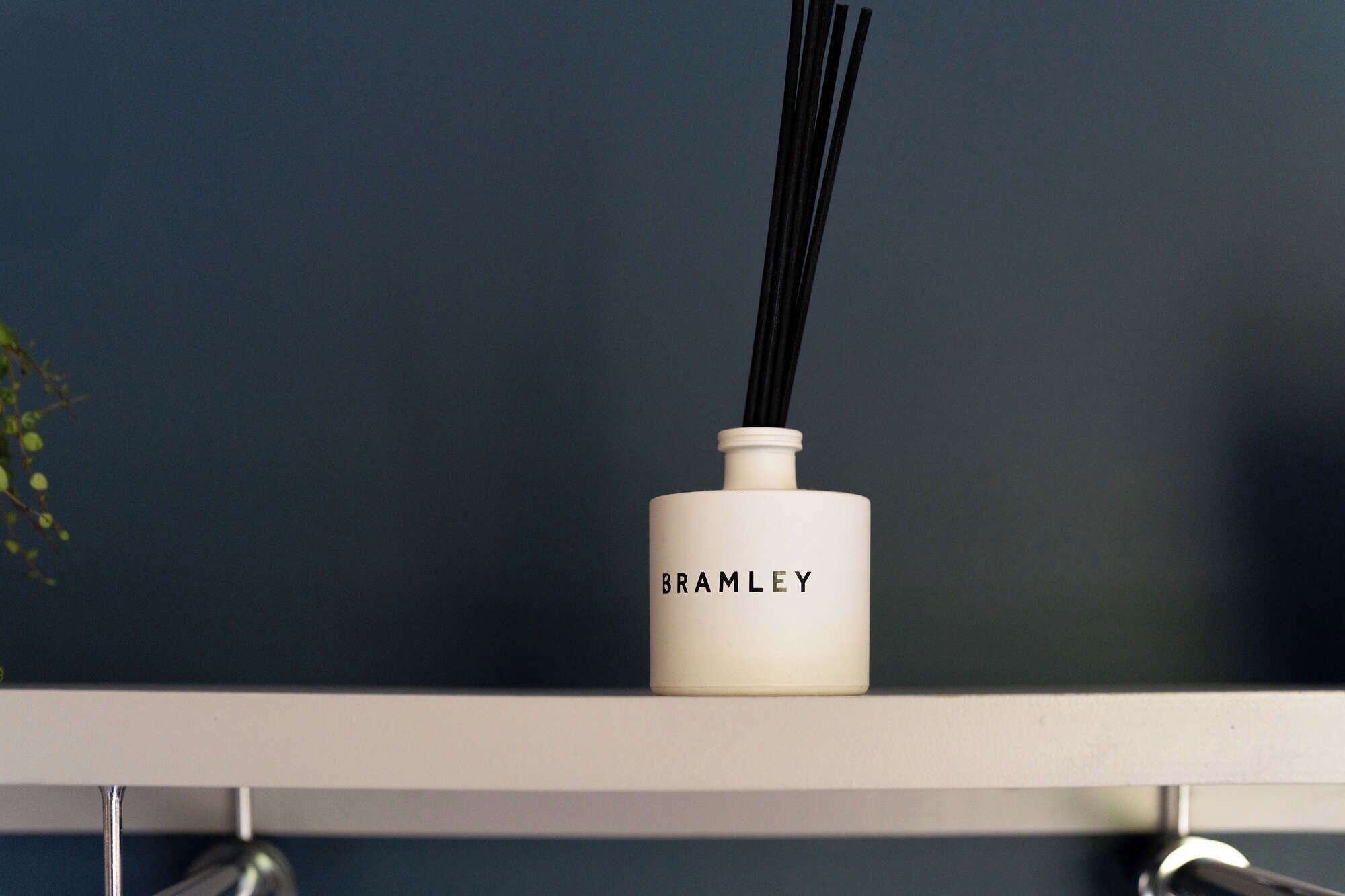 Garrafa branca com a etiqueta 'BRAMLEY' sobre uma prateleira, em frente a um fundo escuro.