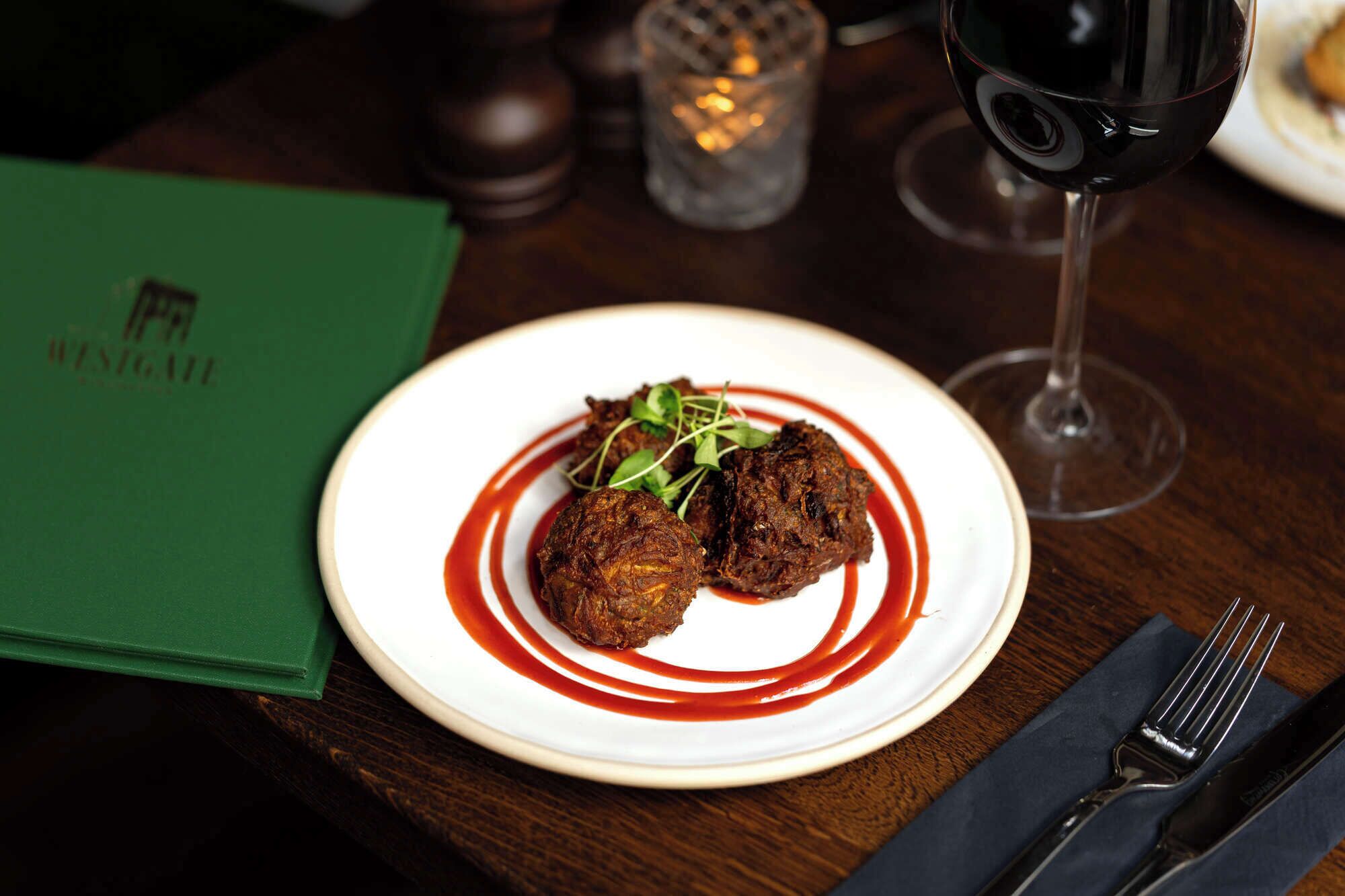 A plate of food with a red sauce, a glass of red wine, and a menu on a table.