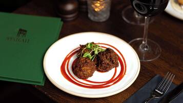 A plate of food with a red sauce, a glass of red wine, and a menu on a table.